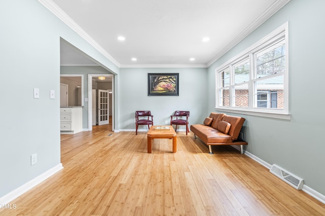 sitting room with light wood-type flooring, baseboards, visible vents, and ornamental molding