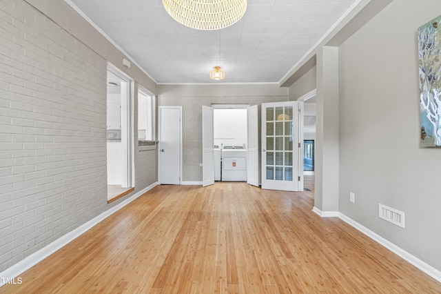 empty room with brick wall, visible vents, light wood-type flooring, washing machine and clothes dryer, and crown molding