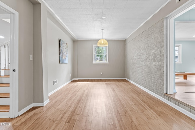 spare room featuring baseboards, brick wall, stairway, crown molding, and light wood-type flooring