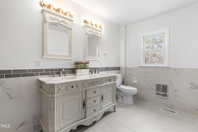 full bathroom with double vanity, a wainscoted wall, tile walls, and a sink