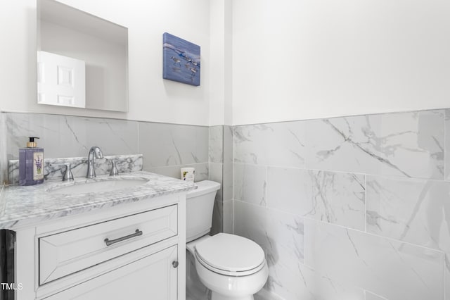 half bathroom featuring tile walls, a wainscoted wall, vanity, and toilet