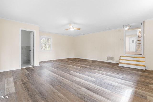 empty room featuring ceiling fan, wood finished floors, visible vents, ornamental molding, and stairway