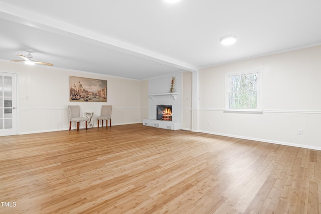 unfurnished living room with a wainscoted wall, ceiling fan, a fireplace, and light wood-style flooring