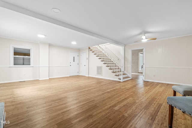 unfurnished living room featuring light wood finished floors, visible vents, ornamental molding, ceiling fan, and stairs