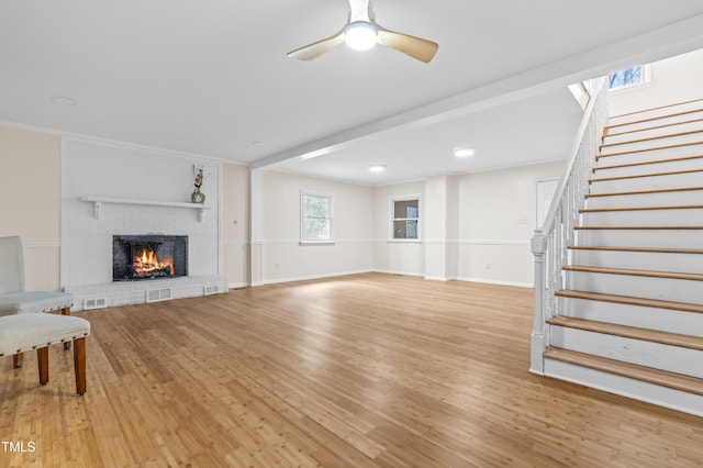 living room with visible vents, a ceiling fan, wood finished floors, stairs, and a brick fireplace