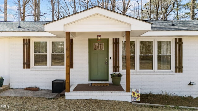 doorway to property with a shingled roof and brick siding