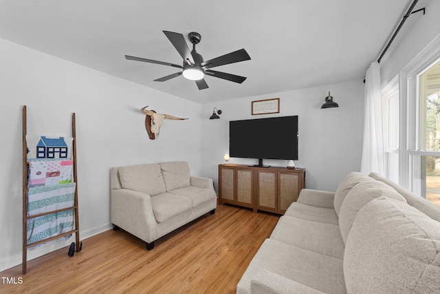 living room with baseboards, a ceiling fan, and light wood-style floors