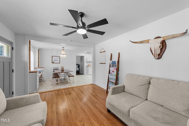 living area with a ceiling fan, light wood-type flooring, and baseboards