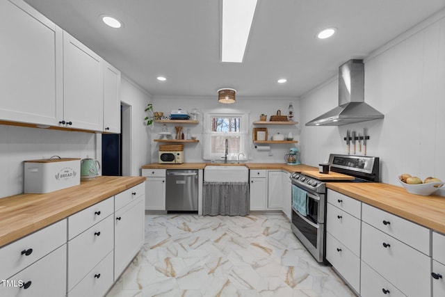 kitchen featuring marble finish floor, open shelves, stainless steel appliances, wall chimney range hood, and butcher block countertops