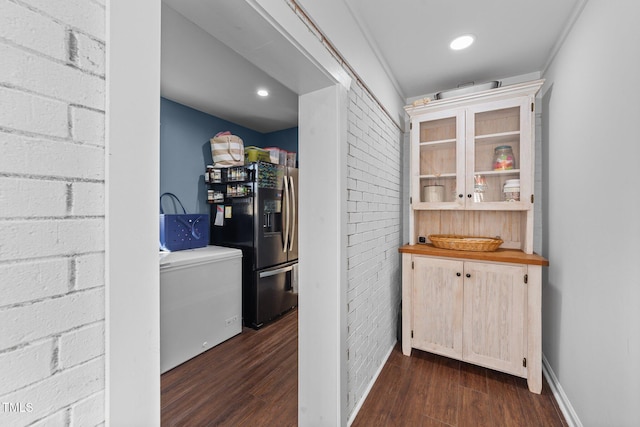 interior space with brick wall, refrigerator with ice dispenser, baseboards, fridge, and dark wood-style floors