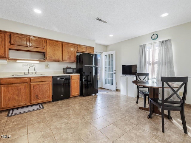 kitchen with black appliances, brown cabinetry, visible vents, and a sink