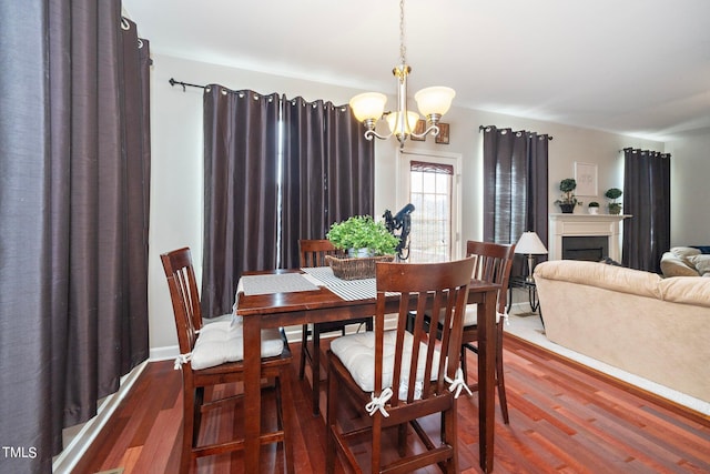 dining area featuring a fireplace, wood finished floors, and a notable chandelier