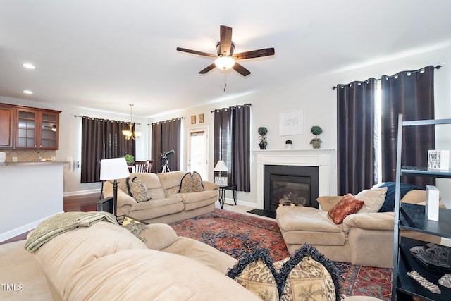 living room featuring a fireplace with flush hearth, recessed lighting, baseboards, and ceiling fan with notable chandelier