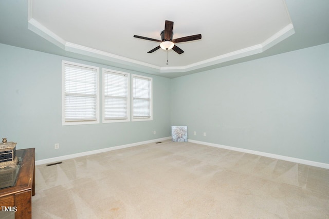 carpeted empty room featuring crown molding, a raised ceiling, visible vents, ceiling fan, and baseboards