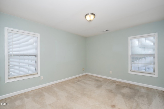 carpeted empty room with baseboards, visible vents, and a wealth of natural light