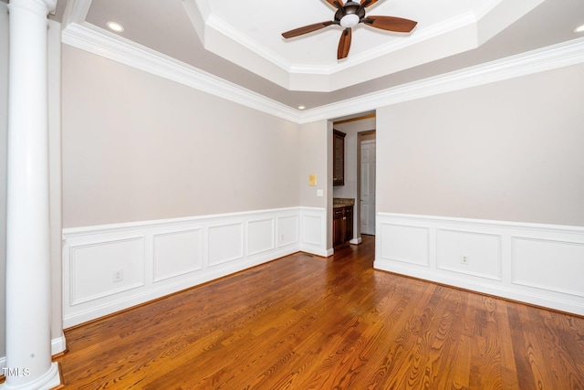 spare room with a tray ceiling, decorative columns, a ceiling fan, ornamental molding, and wood finished floors