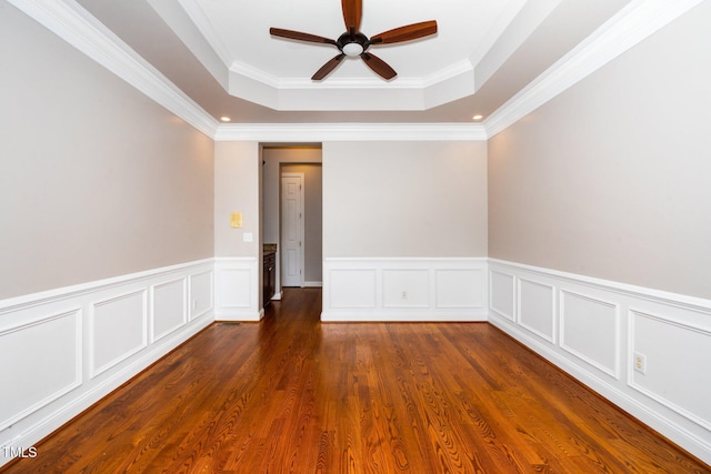 unfurnished room with dark wood-style flooring, a raised ceiling, a ceiling fan, and ornamental molding