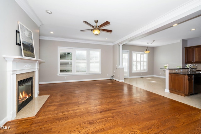 unfurnished living room with ornamental molding, a premium fireplace, a sink, and decorative columns