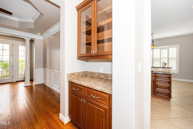 interior space with a healthy amount of sunlight, a wainscoted wall, decorative columns, and crown molding