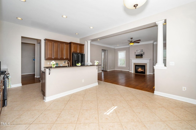 kitchen featuring light tile patterned floors, dark countertops, a glass covered fireplace, black refrigerator, and ornate columns