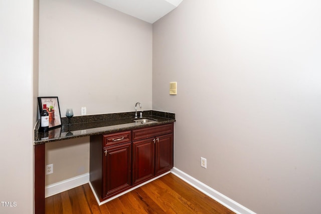 bar featuring baseboards, dark wood finished floors, and a sink