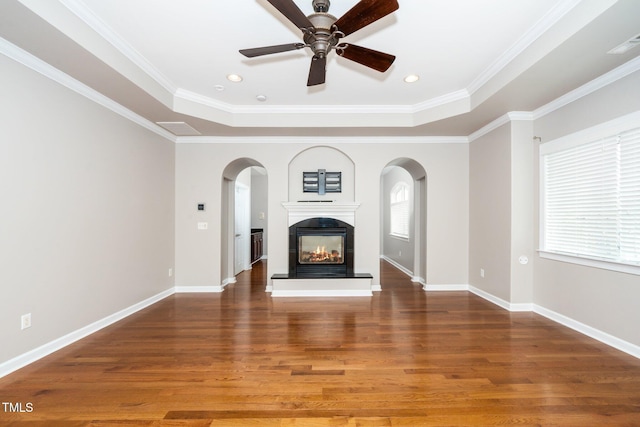 unfurnished living room featuring arched walkways, a tray ceiling, wood finished floors, and a multi sided fireplace