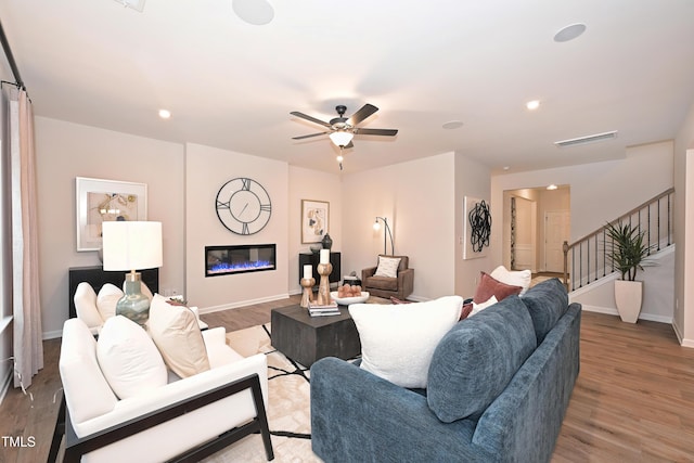 living room with baseboards, visible vents, a glass covered fireplace, wood finished floors, and stairs