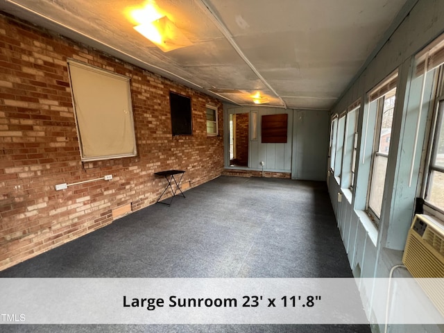 unfurnished living room featuring brick wall