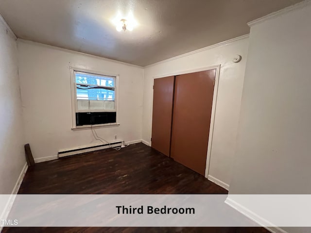 unfurnished bedroom with a baseboard heating unit, crown molding, wood finished floors, and a closet