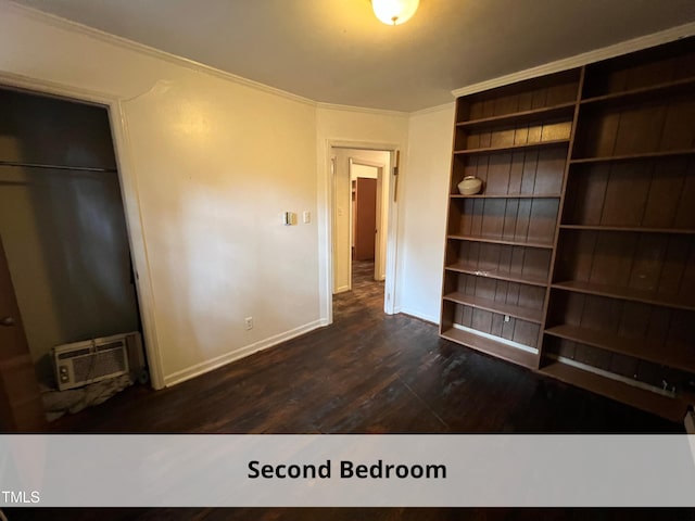 unfurnished bedroom featuring a wall mounted AC, dark wood finished floors, a closet, crown molding, and baseboards