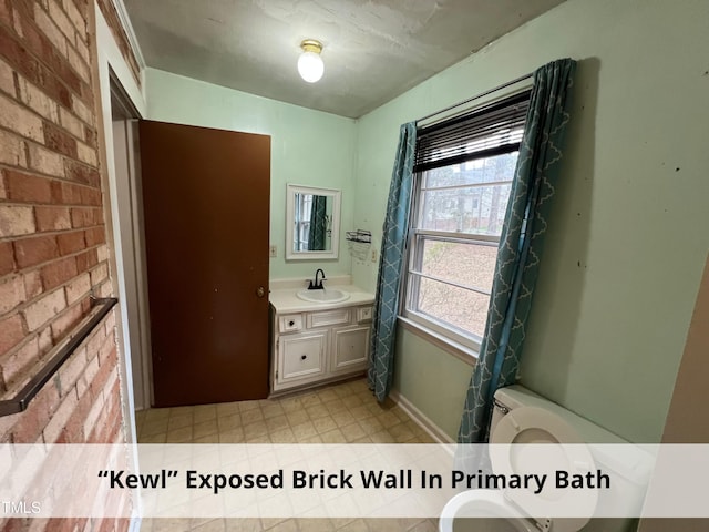 bathroom featuring toilet, brick wall, vanity, and baseboards