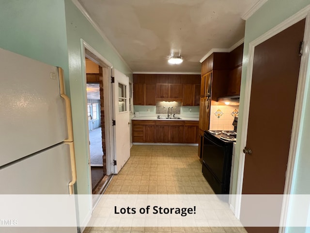 kitchen featuring light floors, freestanding refrigerator, a sink, black electric range, and crown molding