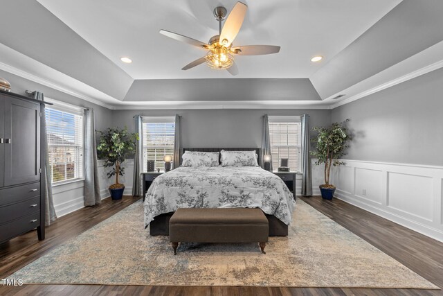 bedroom featuring a tray ceiling, multiple windows, wood finished floors, and a wainscoted wall