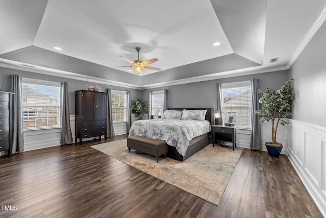 bedroom with a tray ceiling, multiple windows, wood finished floors, and wainscoting