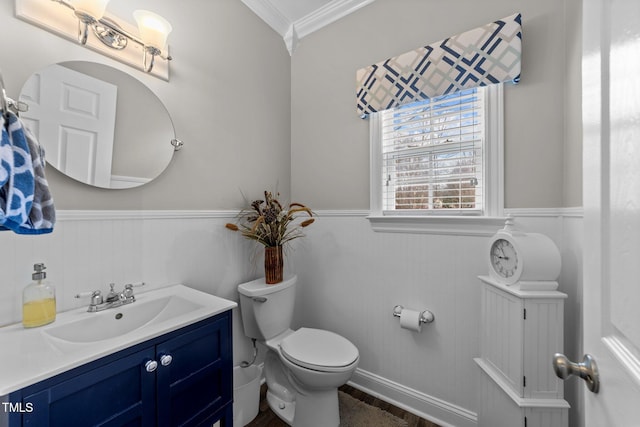 half bathroom with wainscoting, vanity, toilet, and crown molding