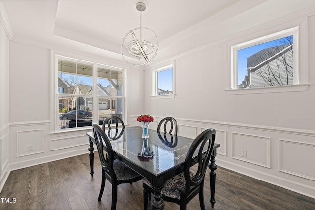 dining space with a tray ceiling, a chandelier, a decorative wall, and dark wood-type flooring