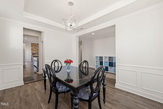 dining room featuring dark wood finished floors, a wainscoted wall, a tray ceiling, a decorative wall, and a notable chandelier