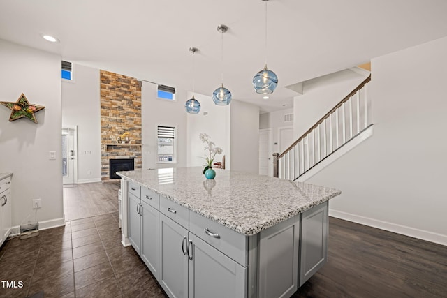 kitchen featuring light stone counters, gray cabinetry, a kitchen island, a stone fireplace, and baseboards