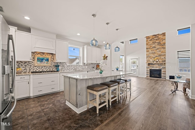 kitchen featuring a stone fireplace, white cabinetry, open floor plan, appliances with stainless steel finishes, and backsplash