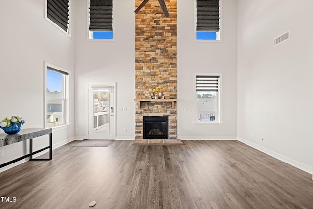 unfurnished living room featuring baseboards, visible vents, wood finished floors, and a stone fireplace