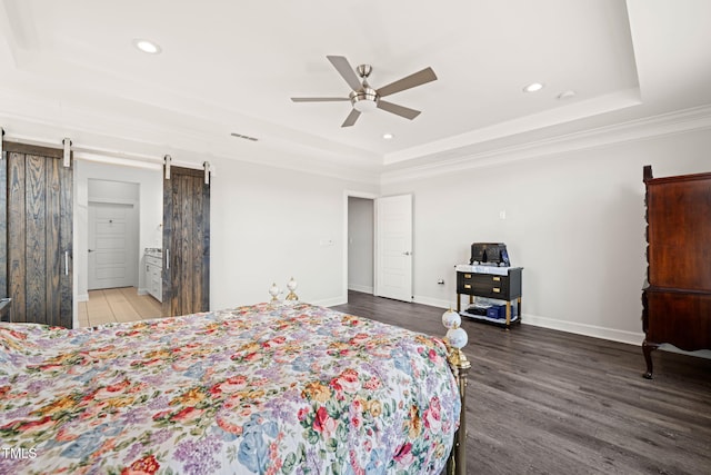 bedroom featuring a barn door, recessed lighting, wood finished floors, baseboards, and a tray ceiling