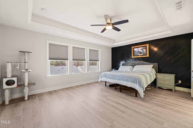 bedroom with a raised ceiling, visible vents, light wood-style floors, an accent wall, and baseboards