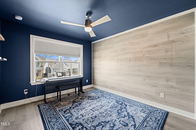 office area featuring wood walls, wood finished floors, a ceiling fan, and baseboards