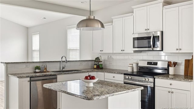 kitchen with light stone counters, stainless steel appliances, a peninsula, a sink, and backsplash