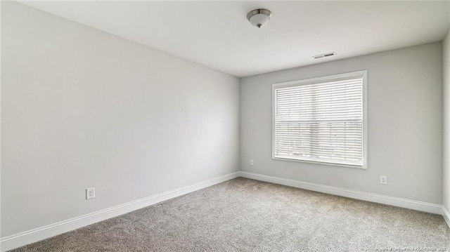 empty room with carpet, visible vents, and baseboards