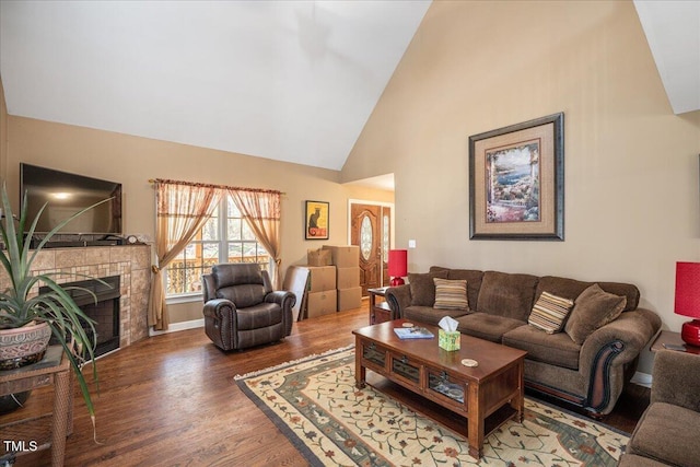 living area featuring high vaulted ceiling, a tiled fireplace, and wood finished floors