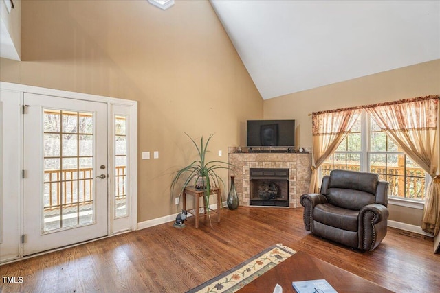 living area featuring high vaulted ceiling, a fireplace, wood finished floors, and baseboards