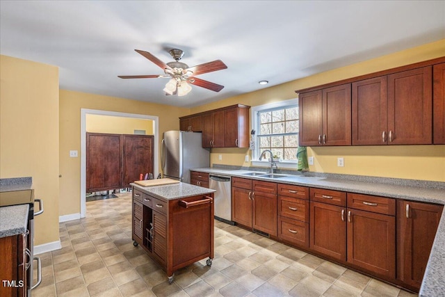 kitchen with stainless steel appliances, light countertops, a sink, a kitchen island, and baseboards