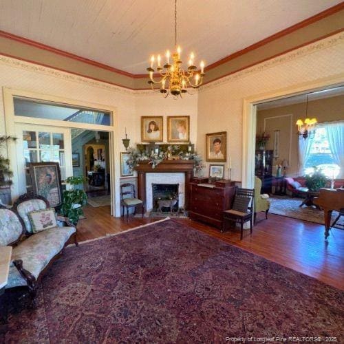 living room featuring crown molding, a fireplace, a notable chandelier, and wood finished floors