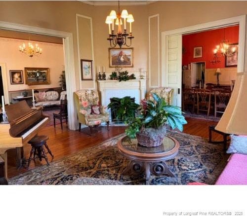 living area with ornamental molding, a fireplace, a notable chandelier, and wood finished floors